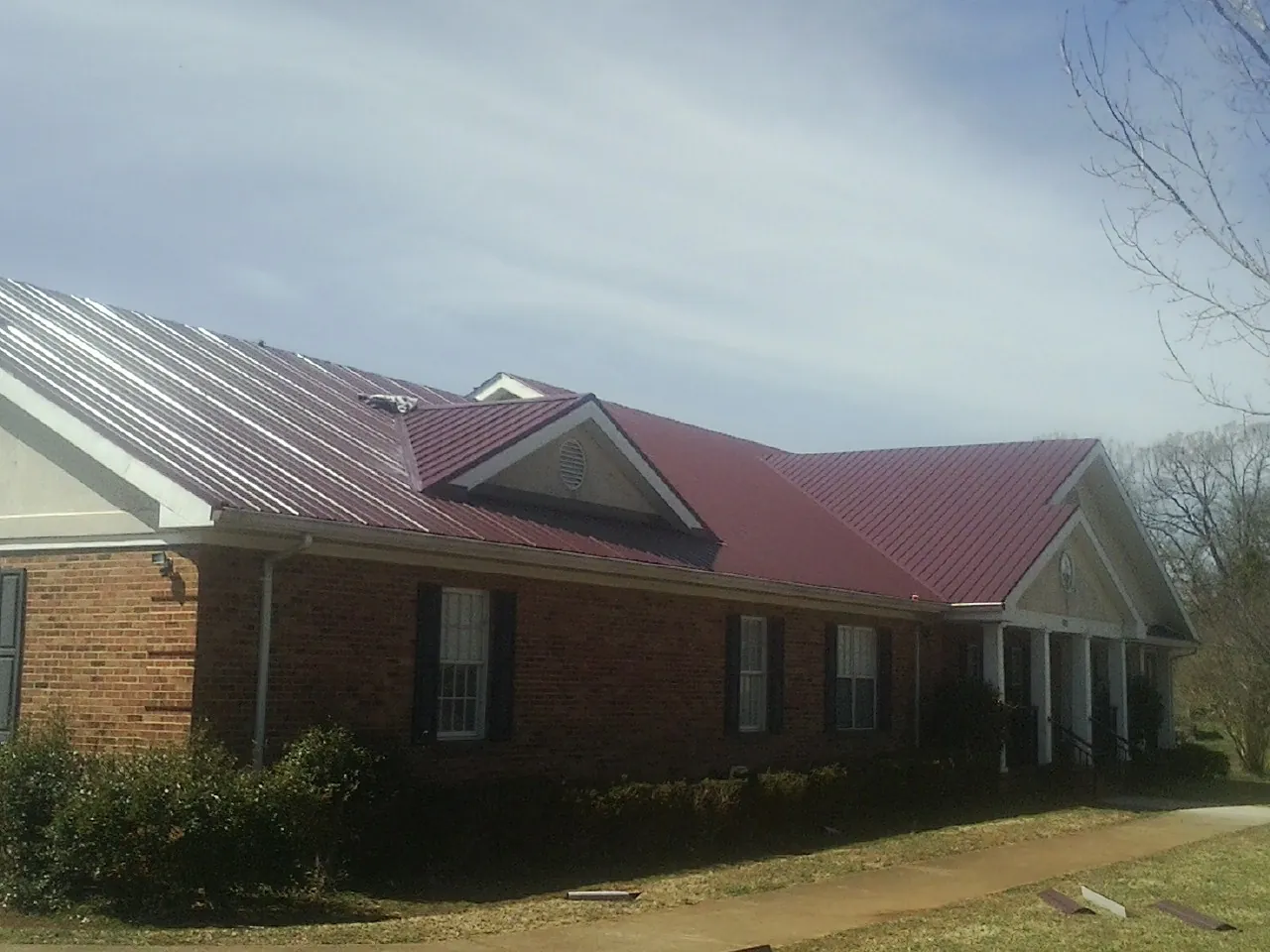 Red metal roof with gabled entries on a long brick building, from a Hail Damage Roof Repair job in New Windsor