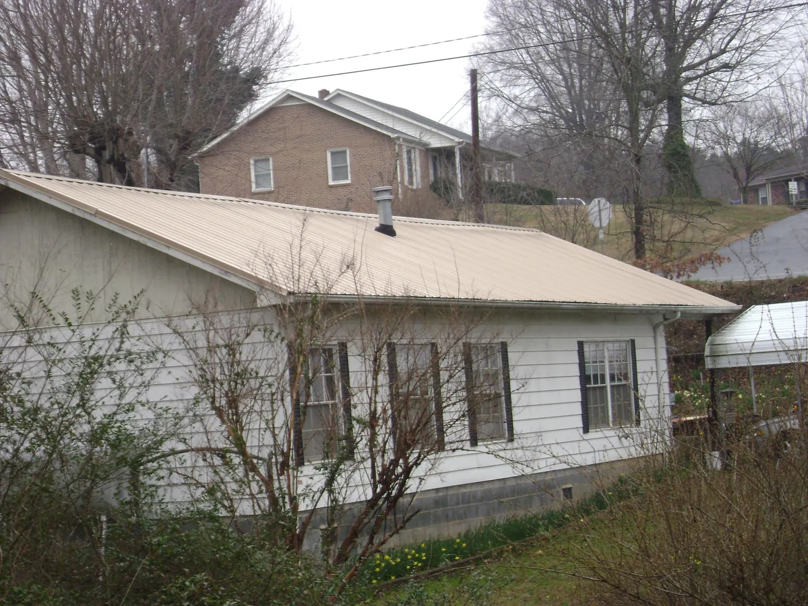 Tan metal roof on a white sided house set into a hillside — Commercial Roofing by Roofing Brothers in New Windsor